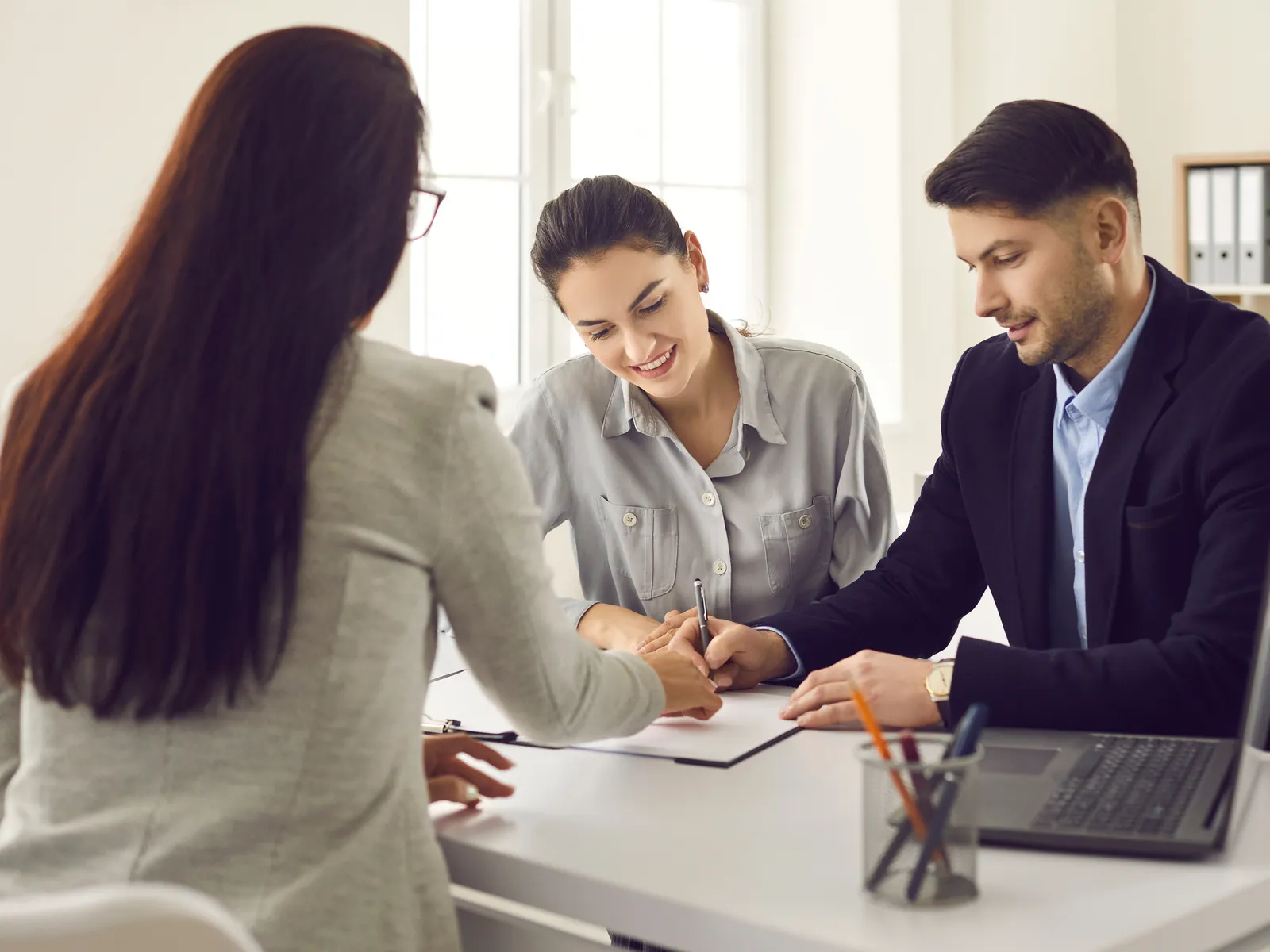 Illustrative image: an agent, seen from behind, reviews a plan with a couple at her desk.
