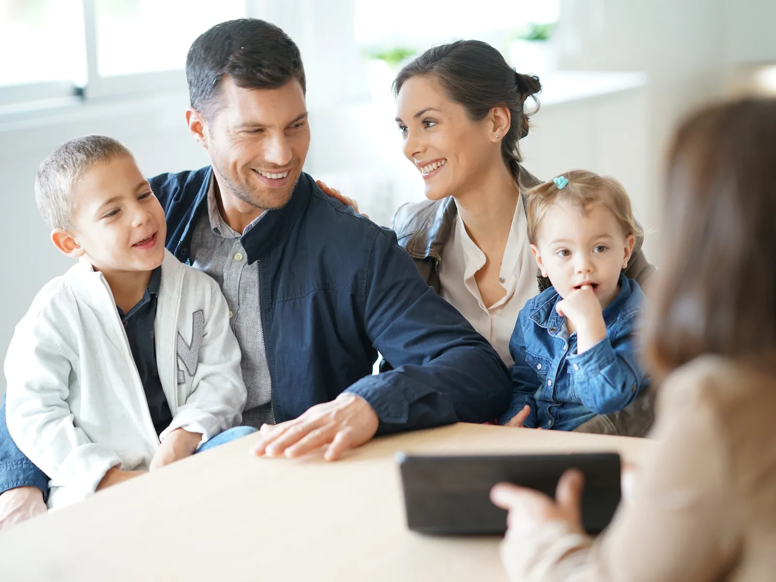 Illustrative image: a couple with two small children, smiling, across the desk from an adviser seen from behind.